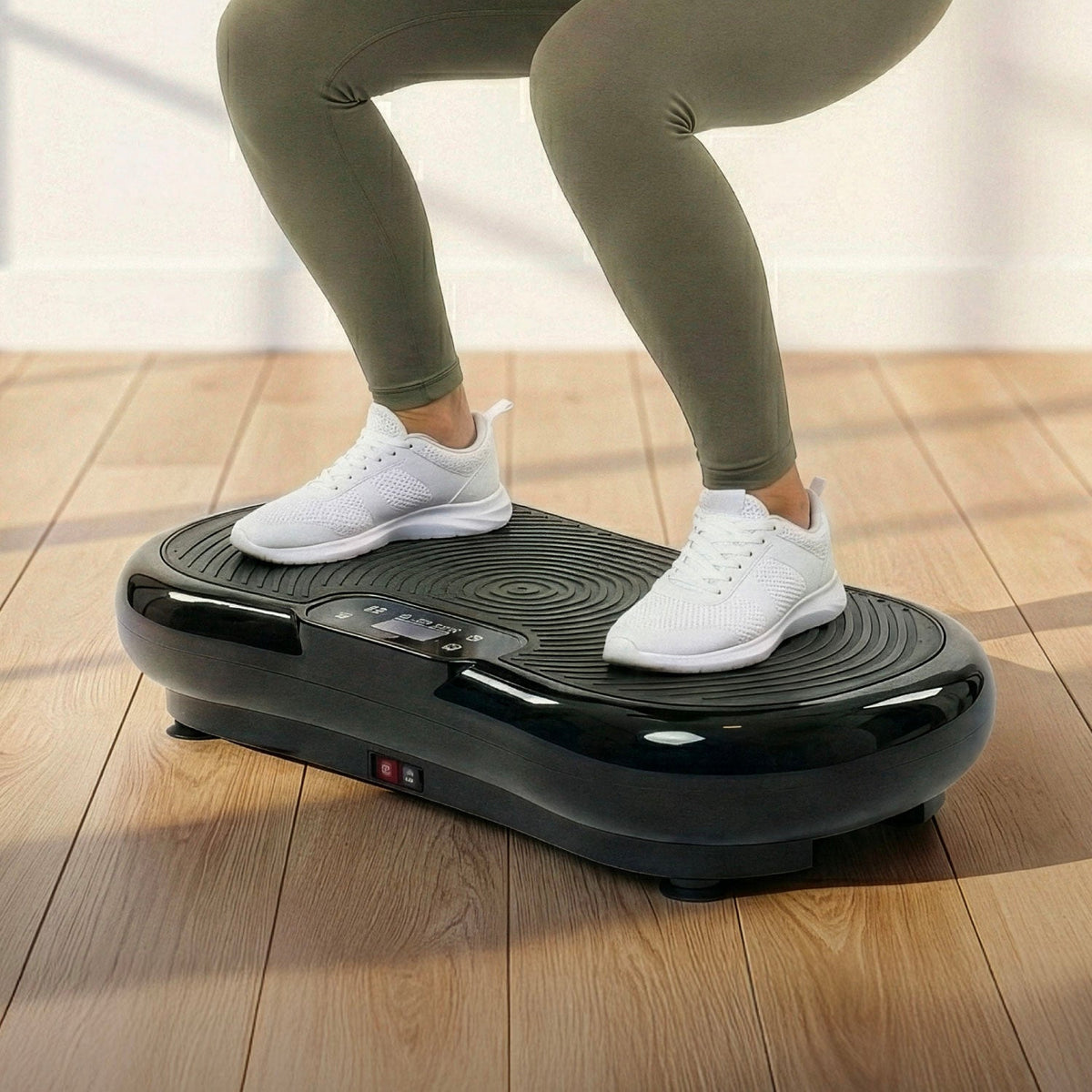 Persona in piedi su una pedana vibrante nera, con scarpe da ginnastica bianche, su un pavimento in legno